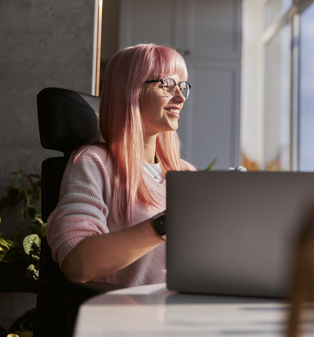 pink-haired-woman-with-elegant-glasses-works-on-laptop-near-window-at-home-e1690441386510